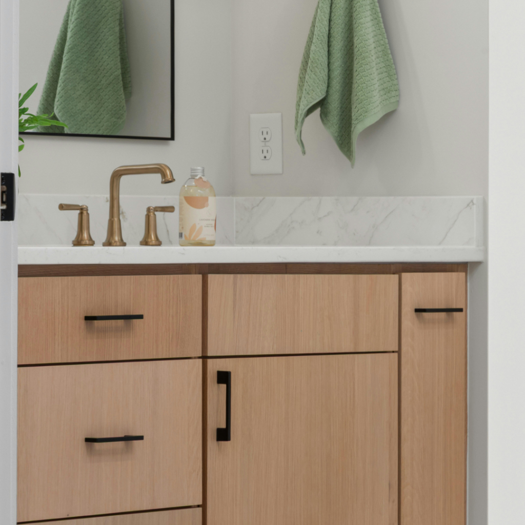 Natural light wood bathroom cabinets with modern black hardware and a gold faucet at a cabinet store in Myrtle Beach, SC.