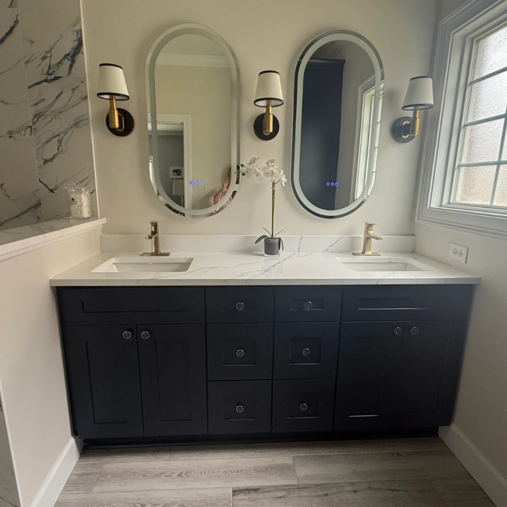 Modern blue bathroom cabinets featuring contemporary backlit LED smart mirrors and gold plumbing fixtures in a coastal home.