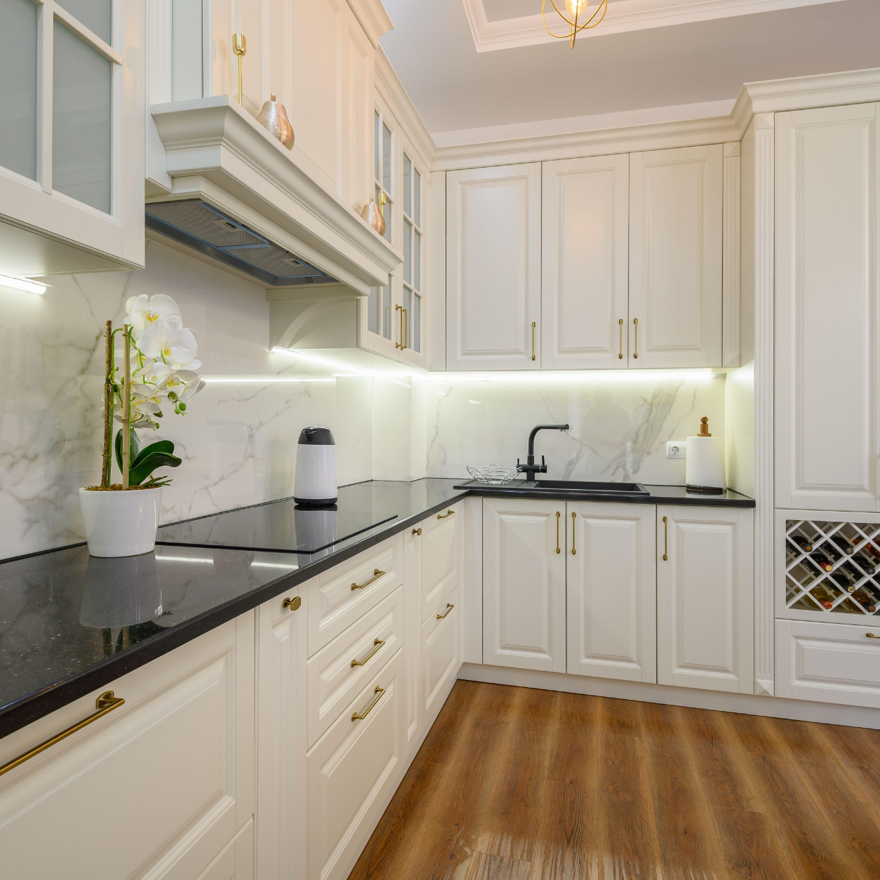 L-shaped off-white shaker kitchen cabinetry with dark countertops, ambient under-cabinet lighting, gold hardware, and a built-in wine rack.